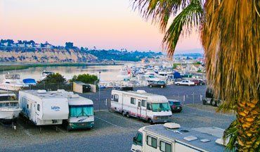RVs in storage area with channel and marina in background at sunset