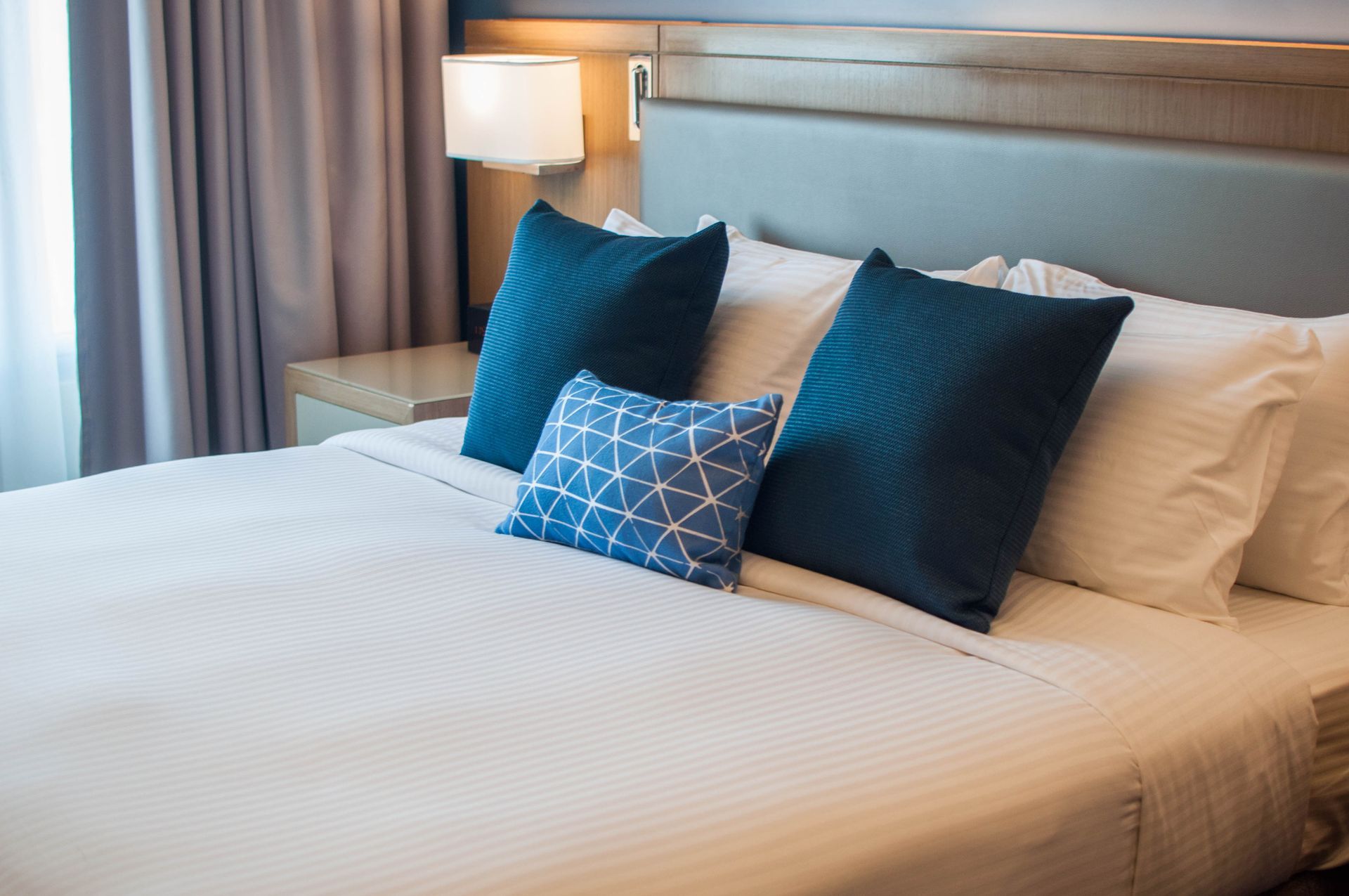 A bed with white sheets and blue pillows in a hotel room.