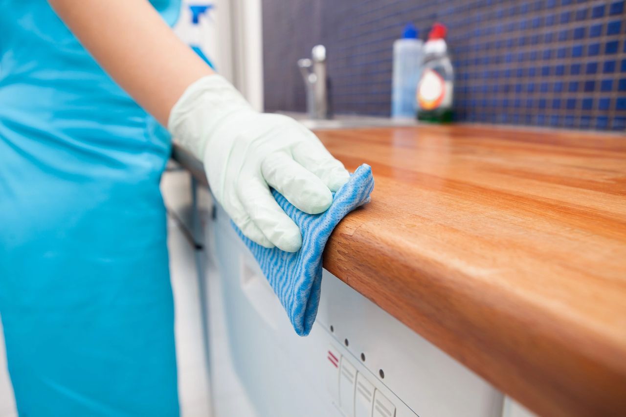 A person is cleaning a kitchen counter with a blue cloth. A person is cleaning a kitchen counter with a blue cloth.