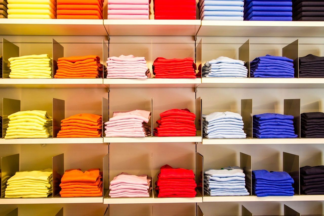 A row of shelves filled with stacks of colorful t-shirts in a store.