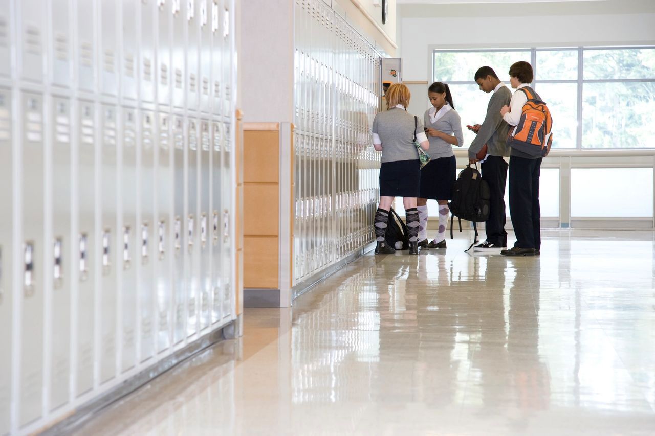 A group of students is standing in a hallway next to lockers. A group of students is standing in a hallway next to lockers.