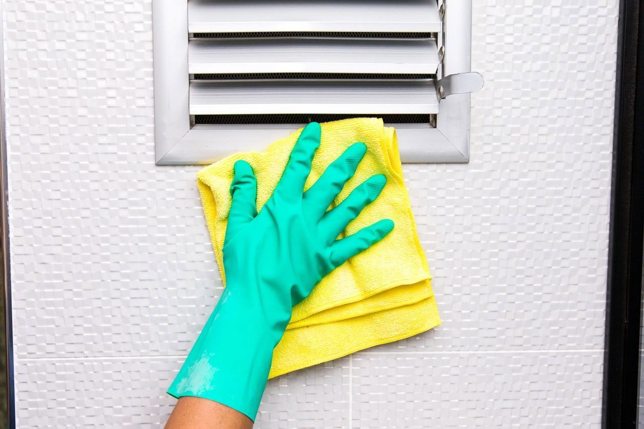 A person wearing green gloves is cleaning a vent with a yellow cloth. A person wearing green gloves is cleaning a vent with a yellow cloth.