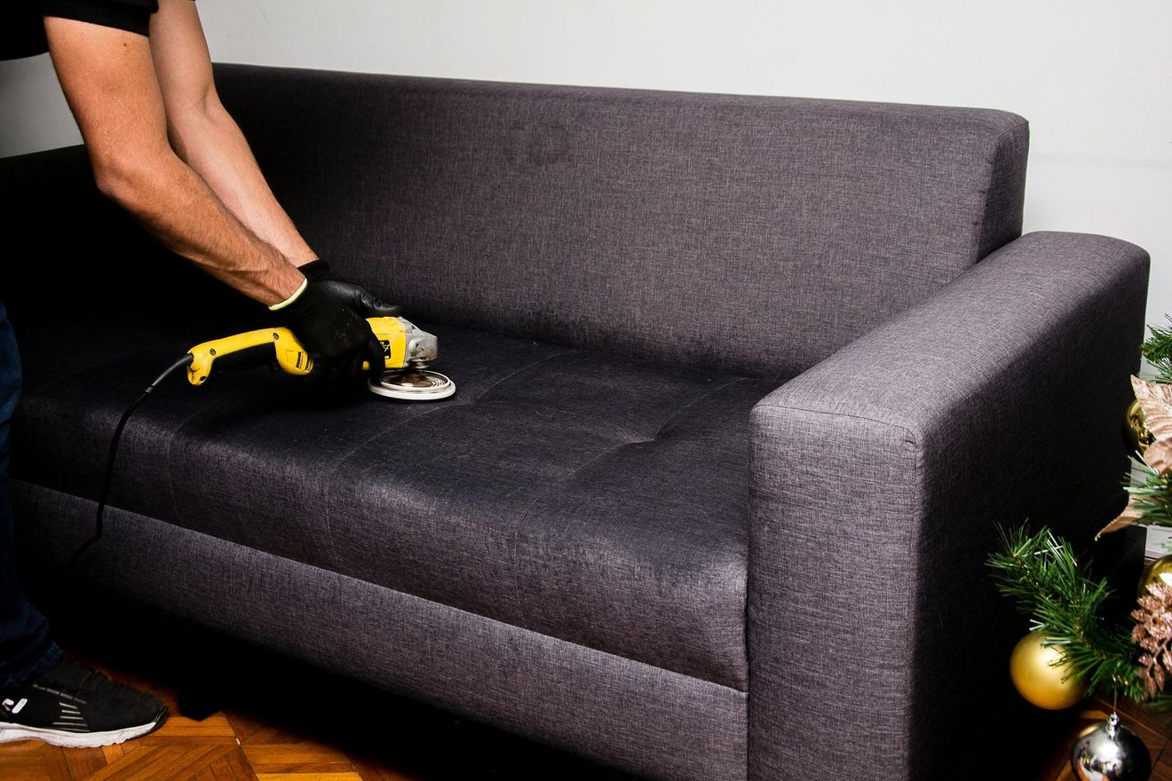 Person using a yellow vacuum to clean a gray couch in a living room