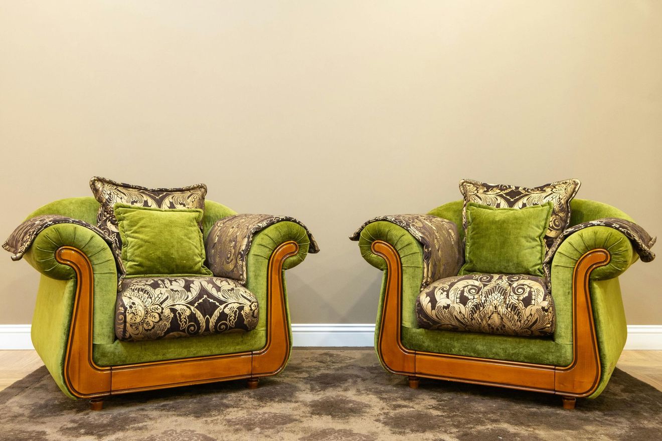 Two ornate green-and-orange armchairs with patterned cushions on a beige carpet against a plain wall