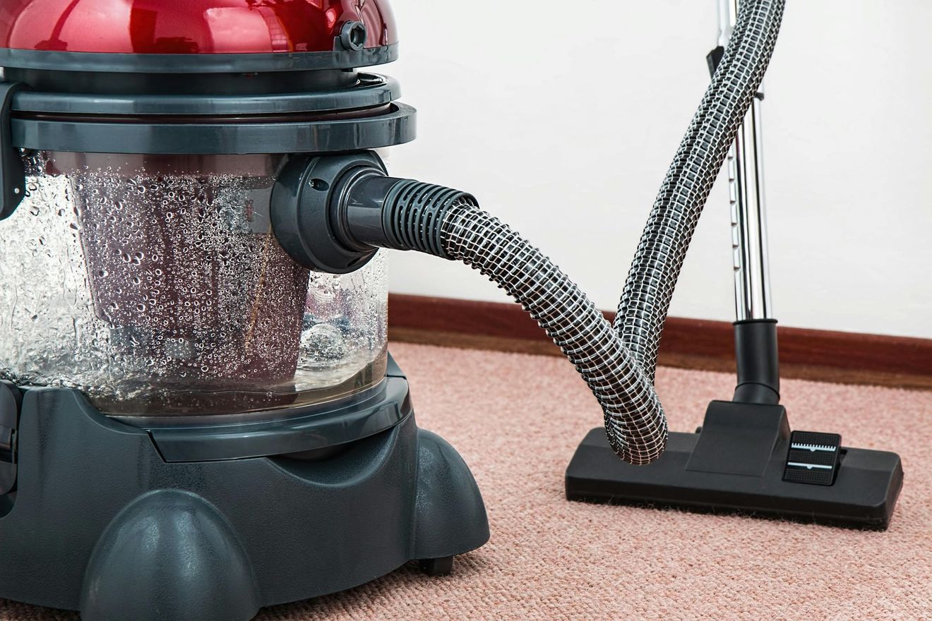Red canister vacuum cleaner with hose and floor nozzle on carpeted floor