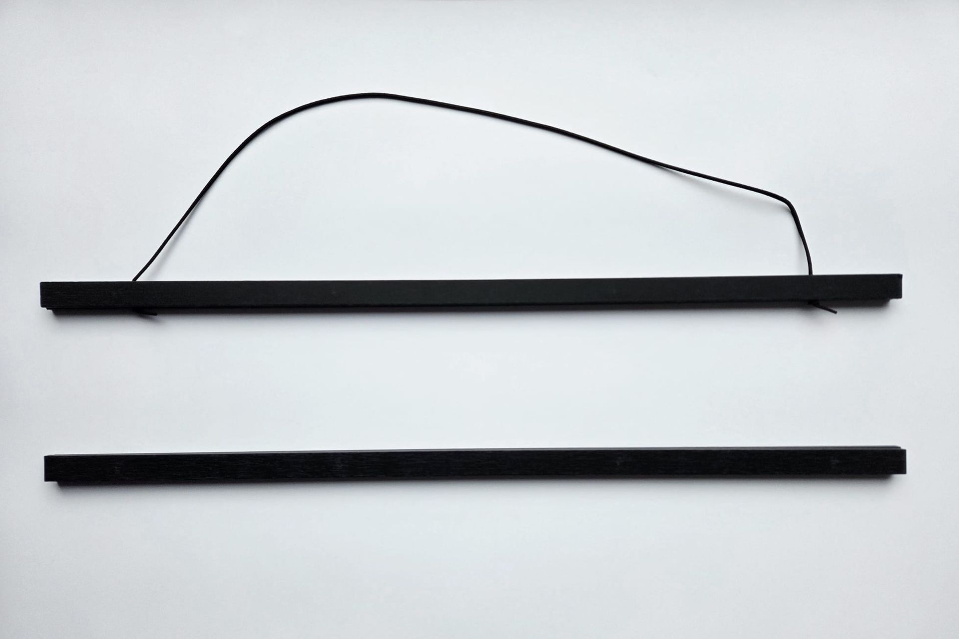 Twee zwarte houten ophangrails voor posters op een witte achtergrond, met een zwart koord aan de bovenste rail om de poster op te hangen.