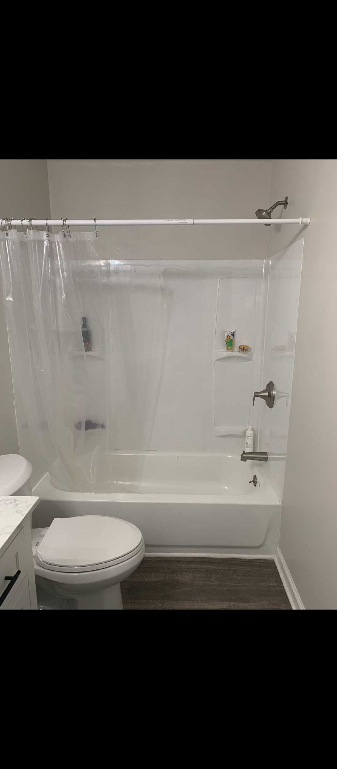 Bathroom with white tub, toilet, and clear shower curtain. Gray floor mat and light gray walls.
