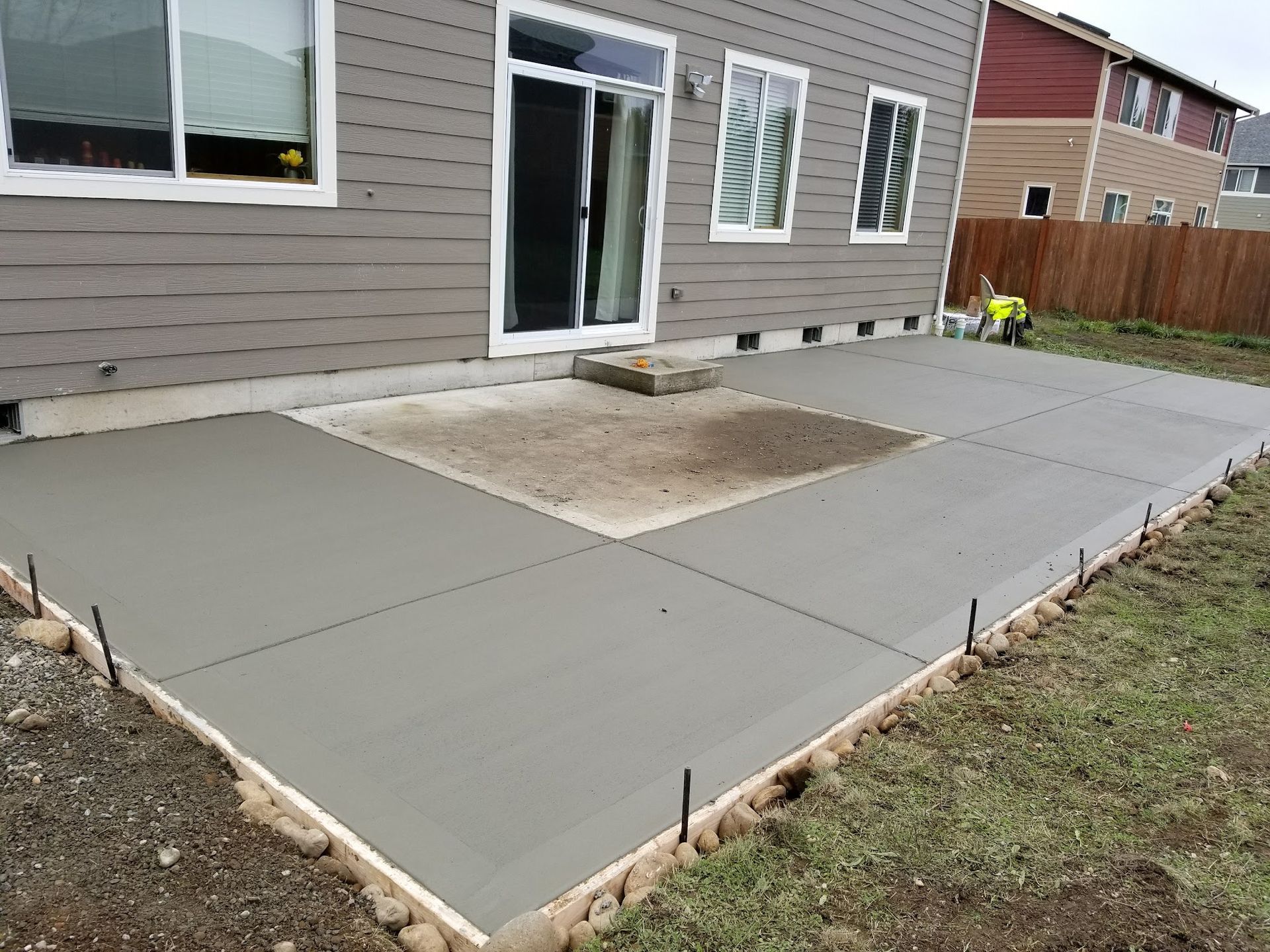 A concrete patio is being built in the backyard of a house.