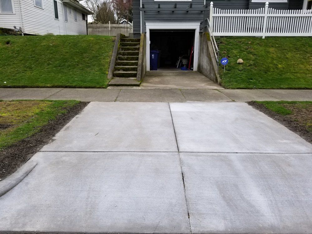 A concrete driveway leading to a garage with stairs leading up to it