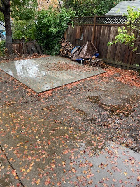 A concrete patio with leaves on it and a wooden fence in the background.