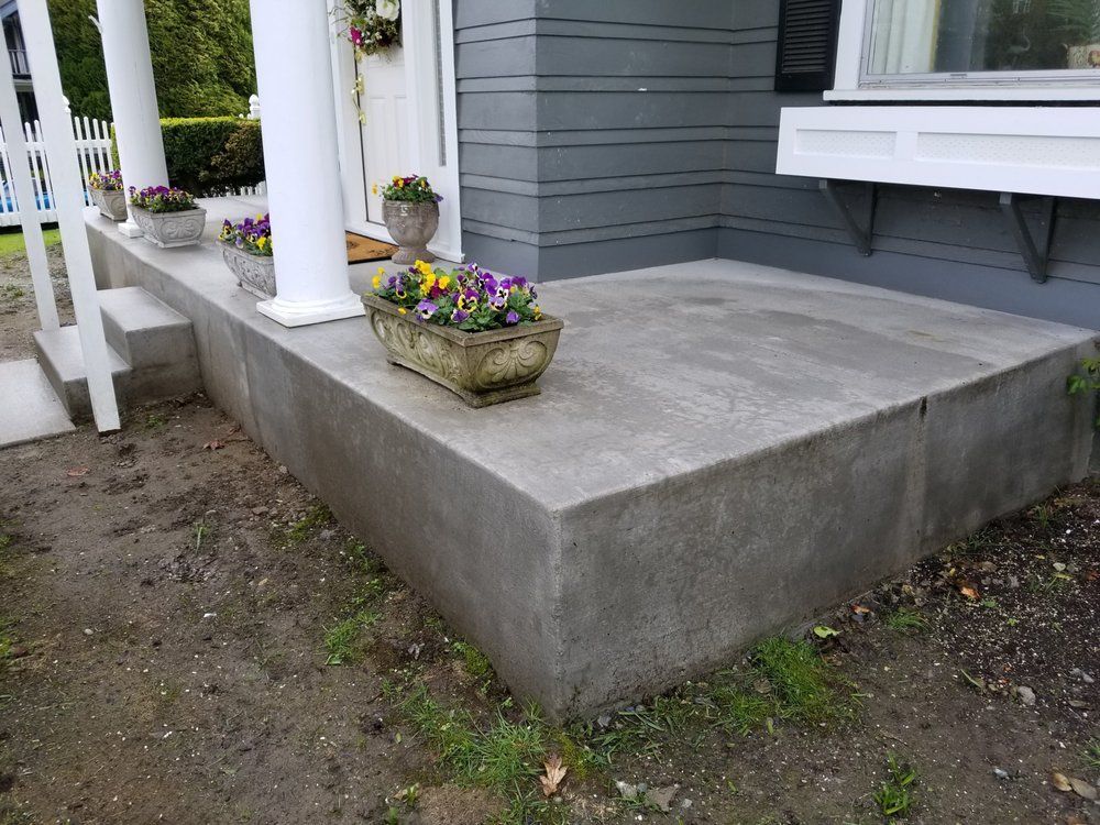 A concrete porch with a planter of flowers on it.