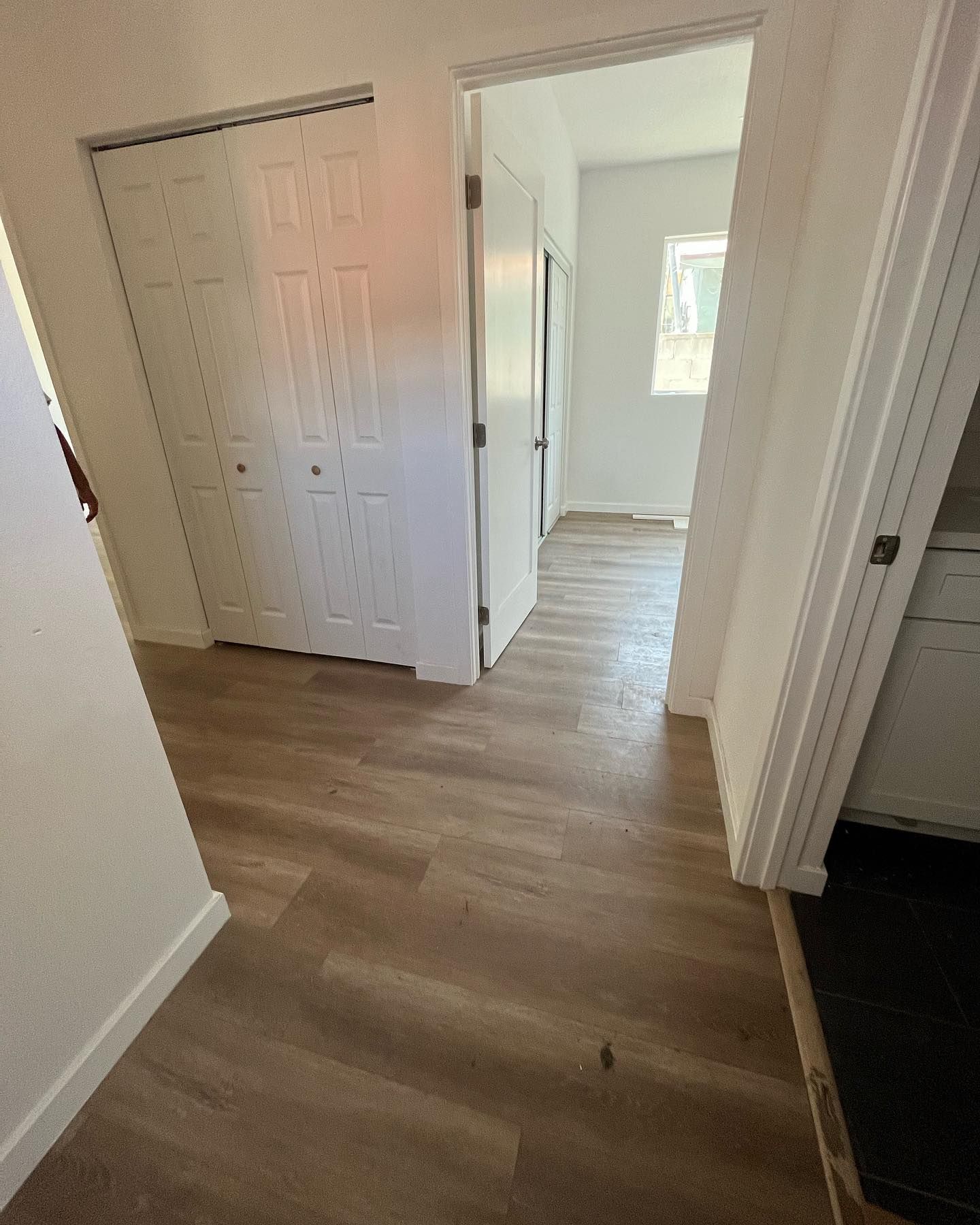 Hallway with light wood-look flooring. White doors lead to closet and room with window.