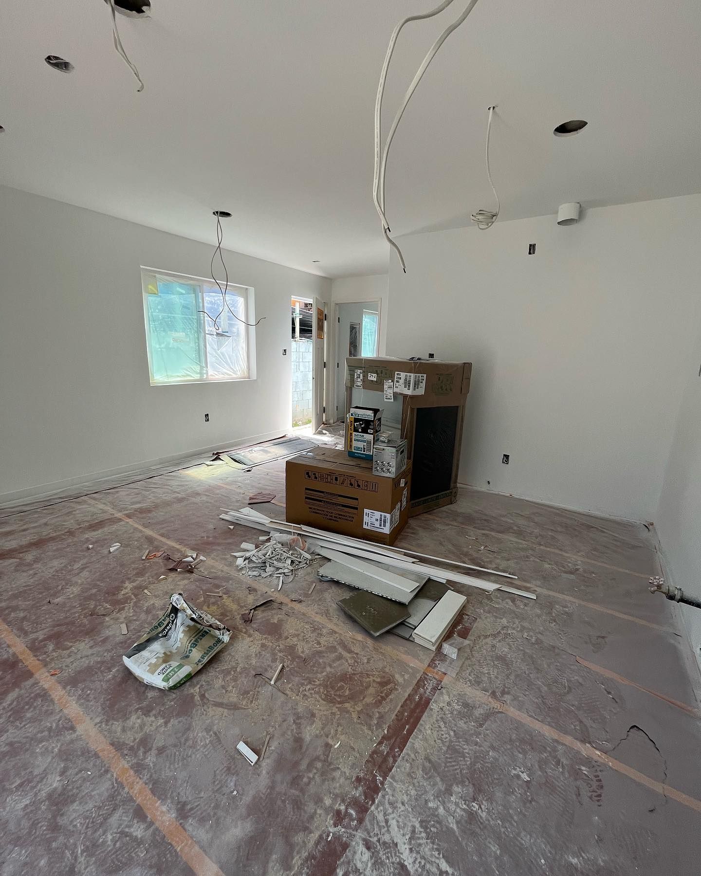 Interior view of room under construction; bare walls, exposed wiring, and debris on the floor.