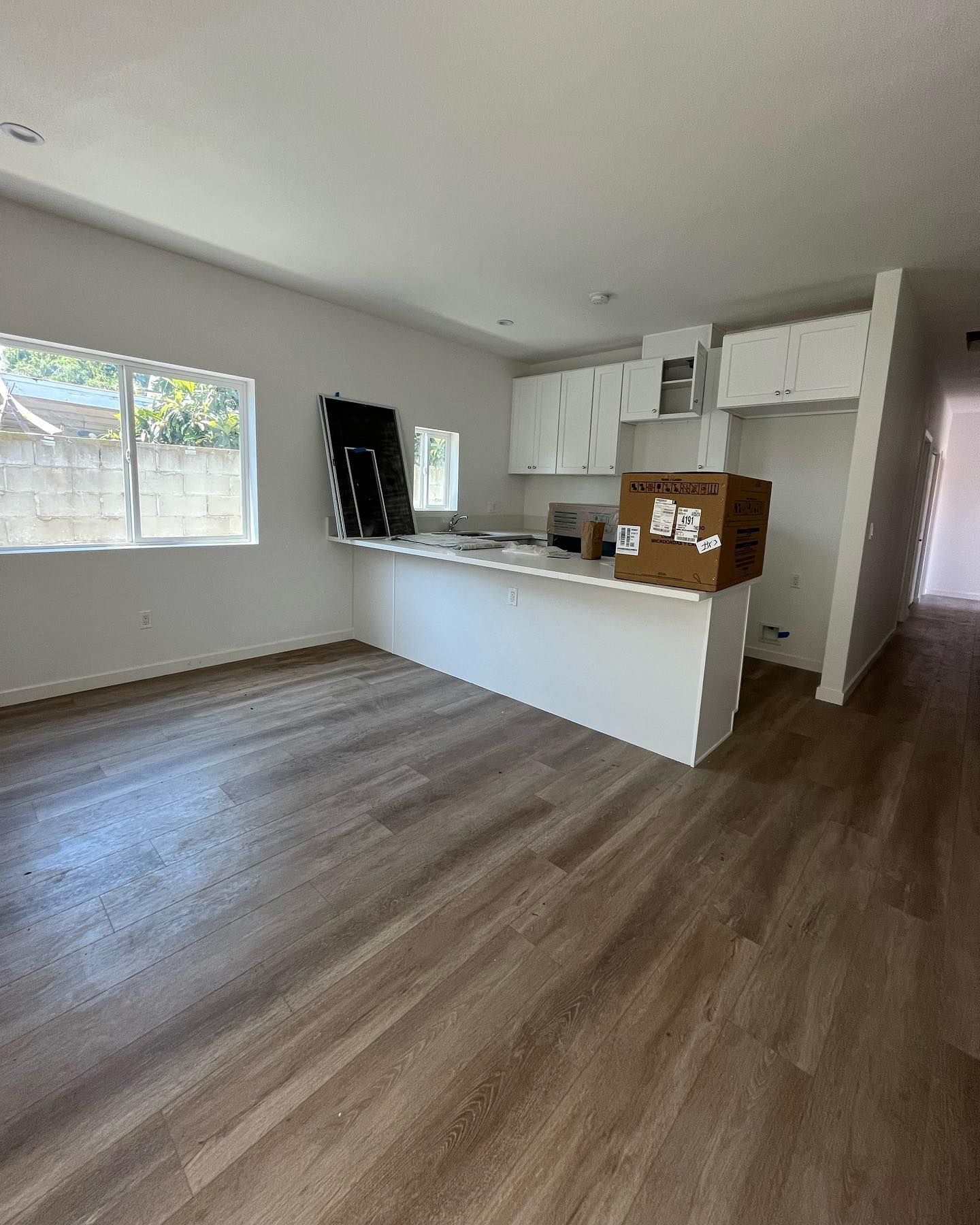 Empty kitchen with white cabinets, island, and wood-look flooring. Natural light streams from window.