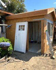 Construction site: new wooden shed with open doorway, white door propped up.