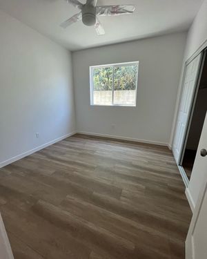 Empty bedroom with wood-look flooring, white walls, a window, sliding closet doors, and a ceiling fan.