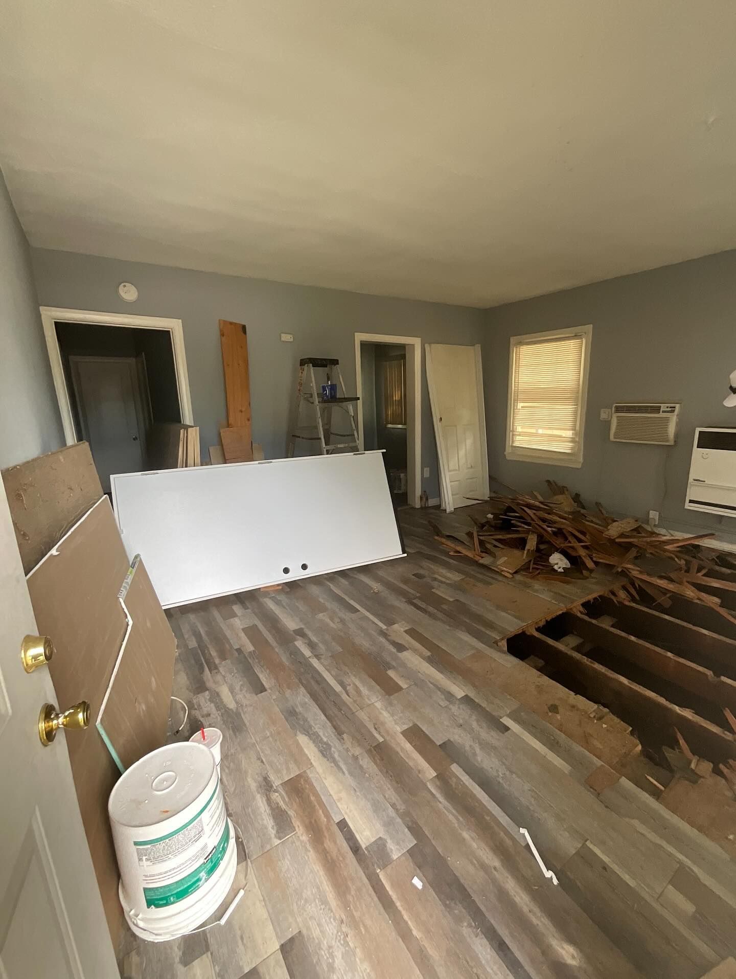 Room with damaged floor and debris, undergoing renovation.