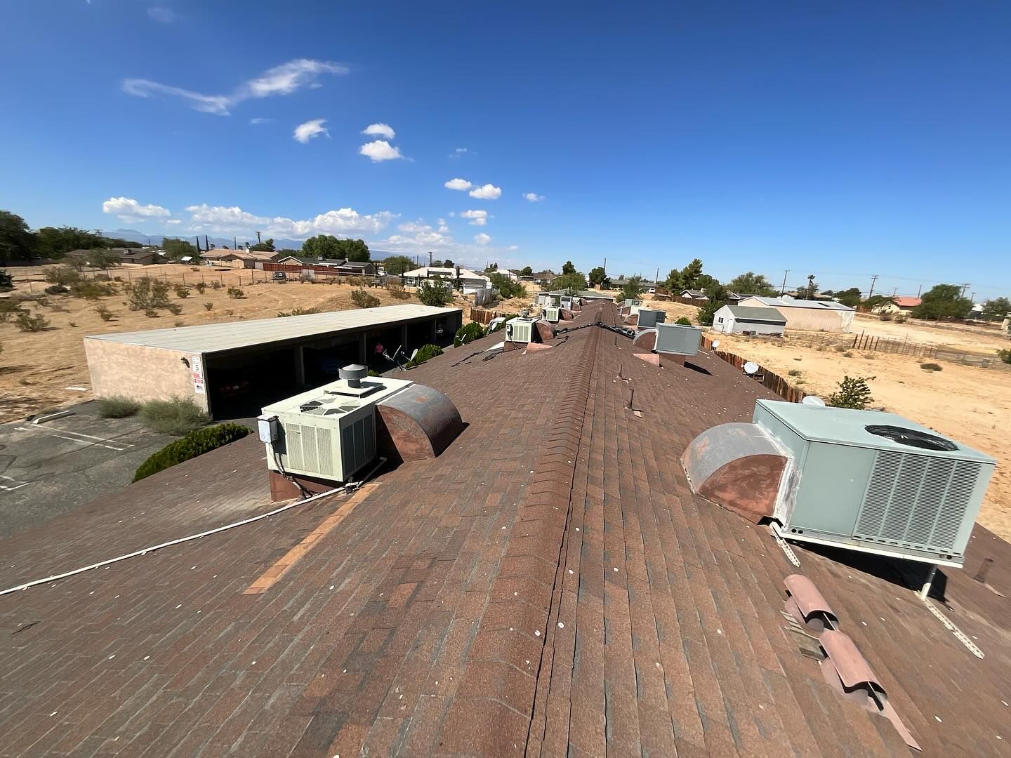 View from a building's weathered roof, several AC units visible, dry landscape, blue sky.