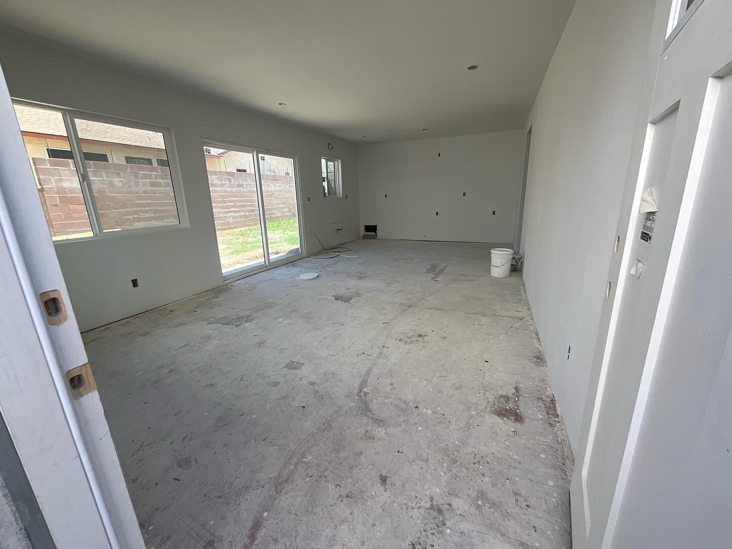Empty room with white walls, unfinished concrete floor, sliding glass door, and window.