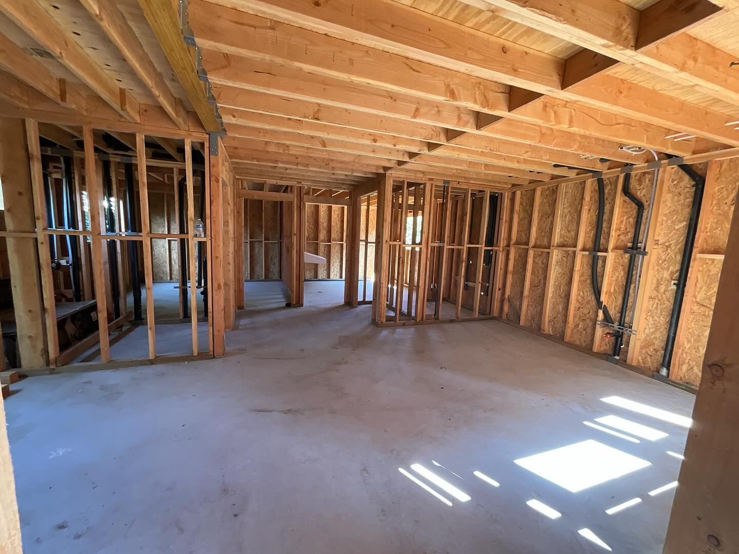 Interior of a house under construction; wooden framing, concrete floor, sunlight.