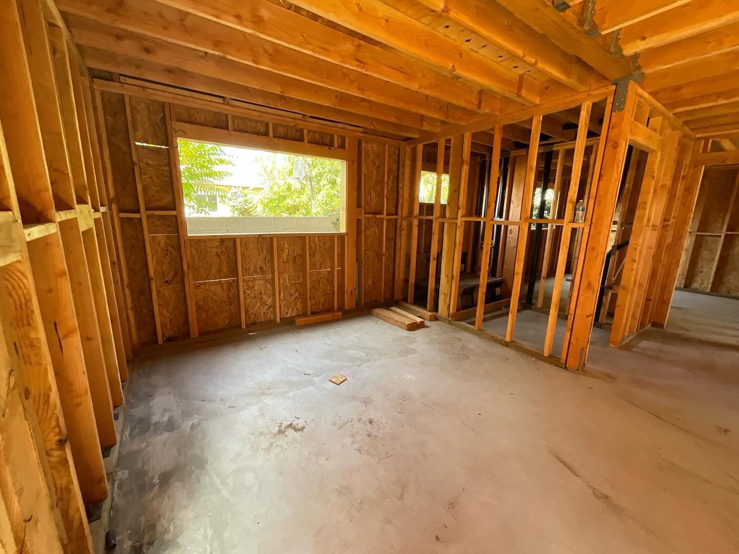 Interior of a room under construction, with wooden frame walls, a window, and a concrete floor.