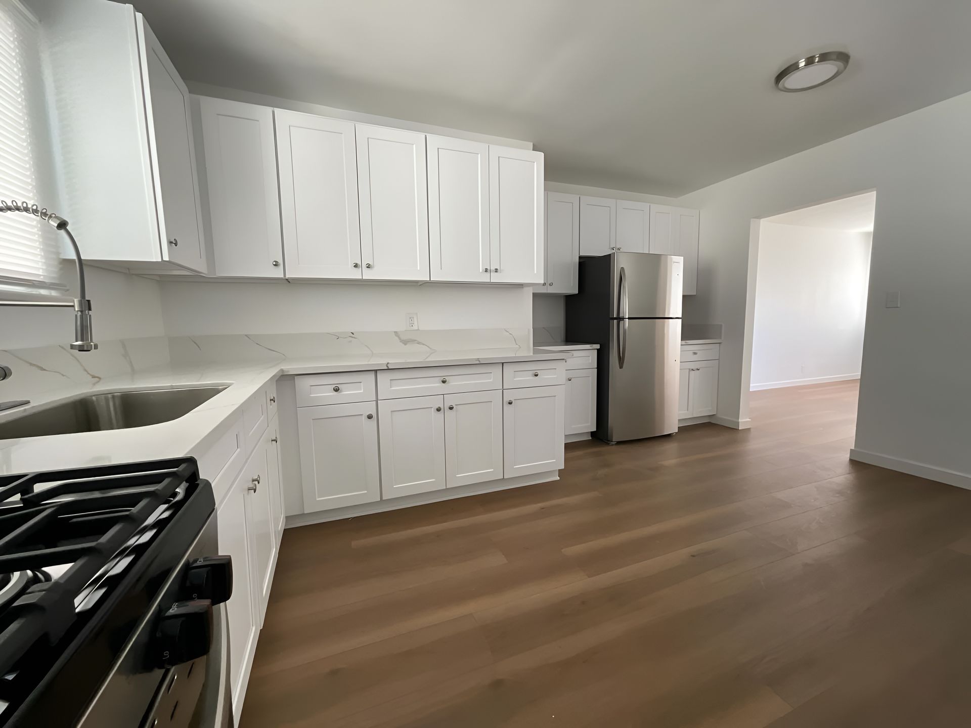 White kitchen with cabinets, countertops, appliances, and wood flooring.