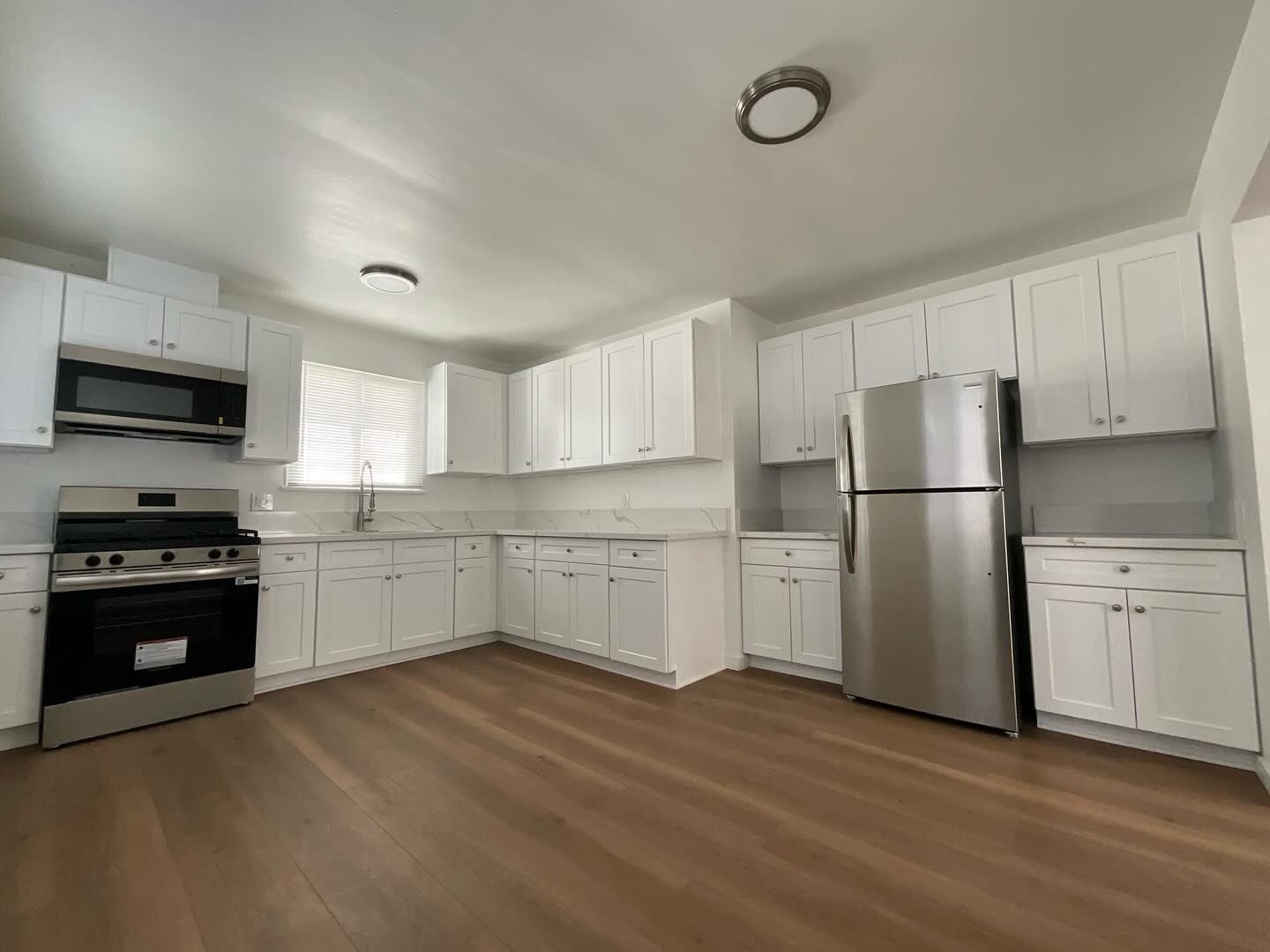 White kitchen with stainless steel appliances and light brown flooring.