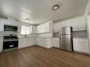 White kitchen with stainless steel appliances and light brown flooring.