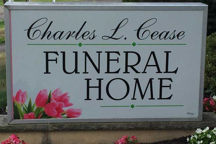 Sign for Charles L. Cease Funeral Home. Features text, flowers, and a light-colored background.