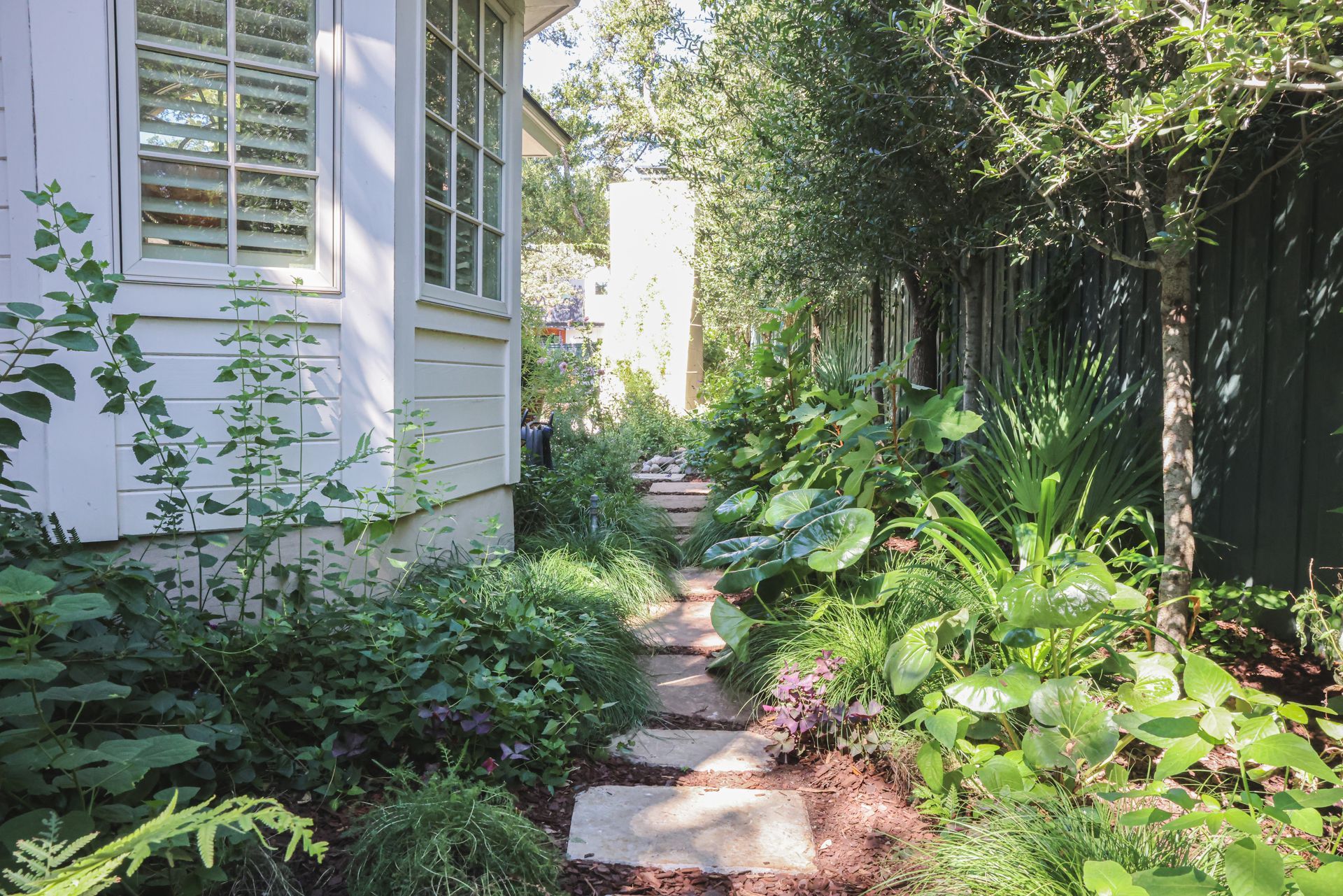 A stone path leading to a house surrounded by trees and plants.