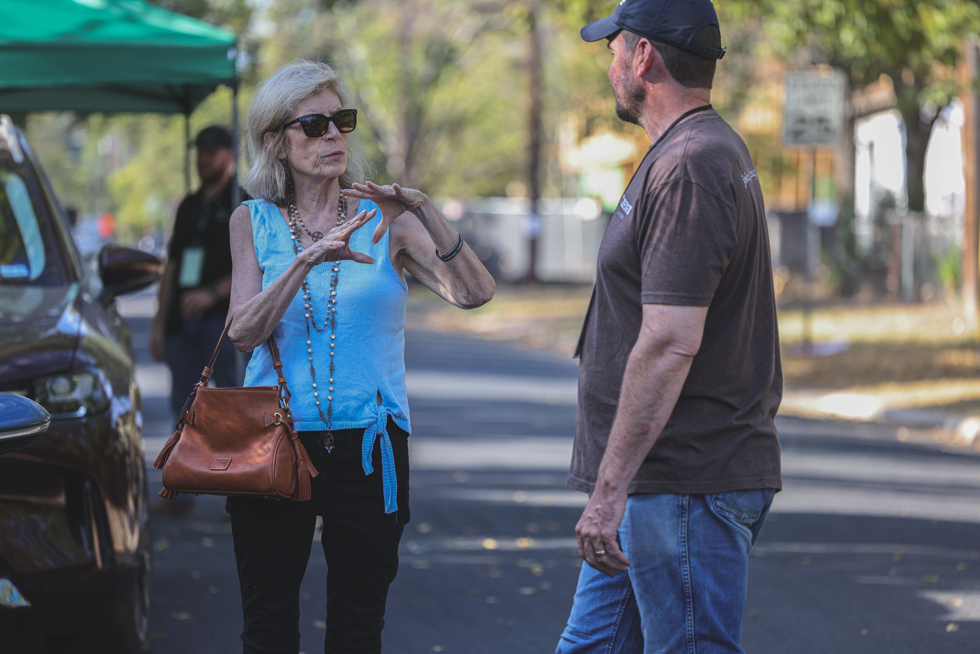 A man and a woman are standing on the side of the road talking to each other.
