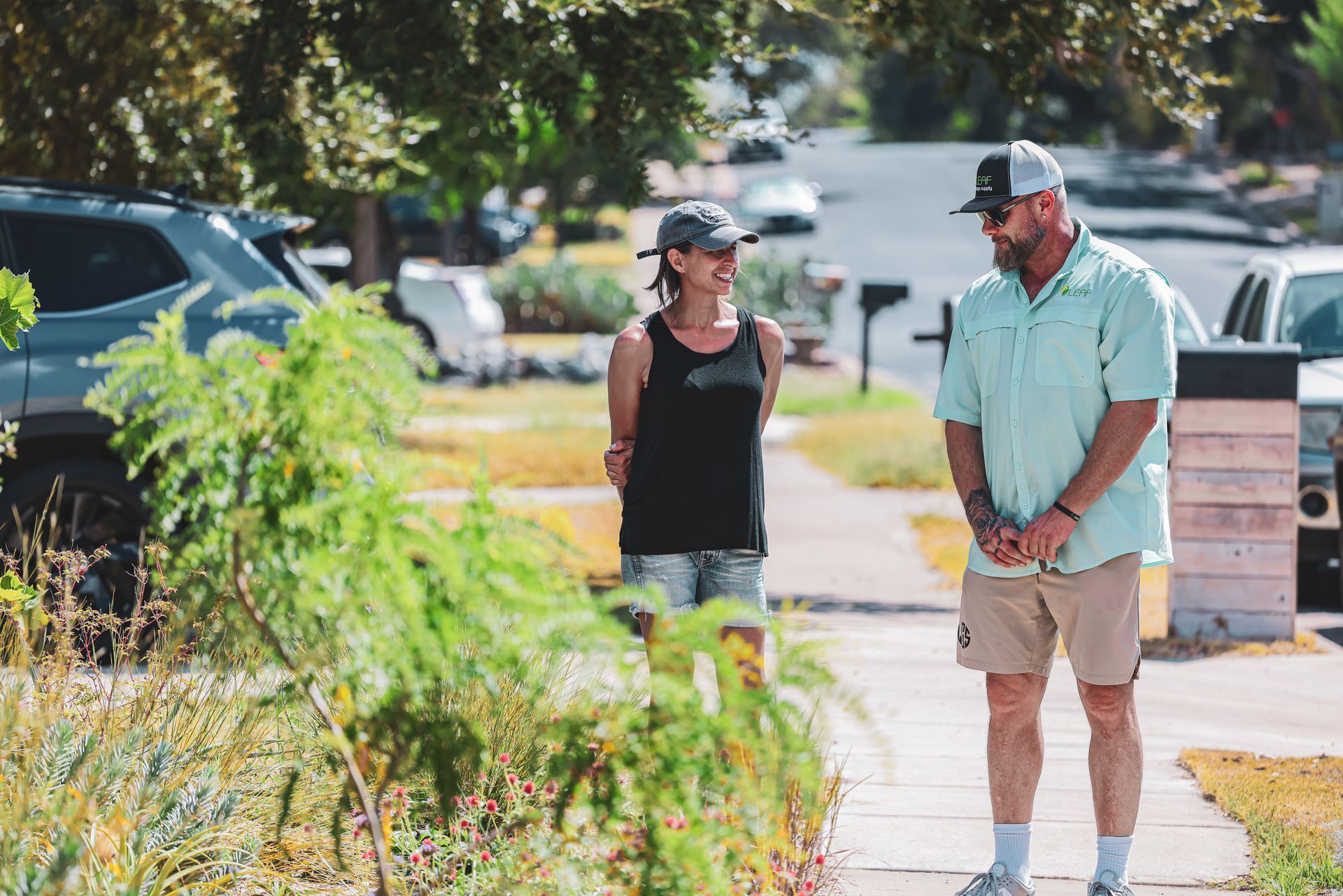 A man and a woman are standing on a sidewalk talking to each other.