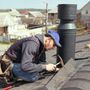 A roofing contractor is kneeling on a roof working on a chimney.