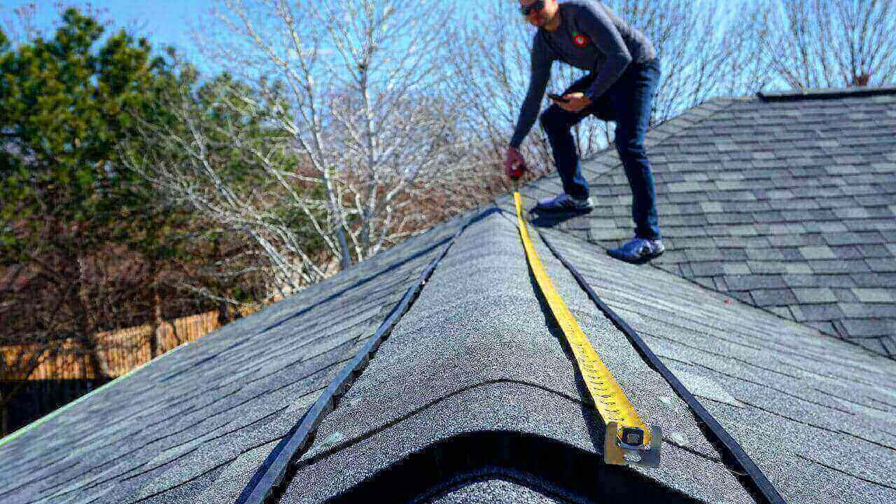 A man using a tape measure to measure the roof of a building.