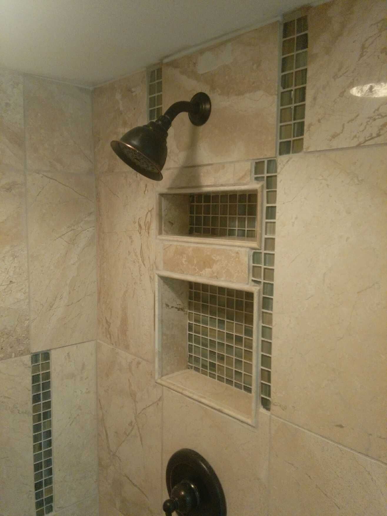 Shower interior with beige tile and built-in shelving, dark showerhead and fixtures, accented with mosaic tile strips.