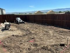 A backyard with a wooden fence and a bulldozer in the dirt.