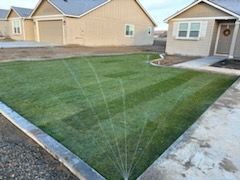 A sprinkler is spraying water on a lush green lawn in front of a house.
