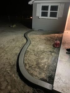 A concrete curb is being installed in front of a house at night.