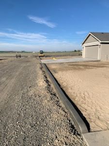 A dirt road with a concrete curb and a house in the background.