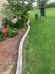 A concrete curb is being installed in a backyard next to a swing set.