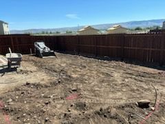 A backyard with a wooden fence and a bulldozer in the dirt.