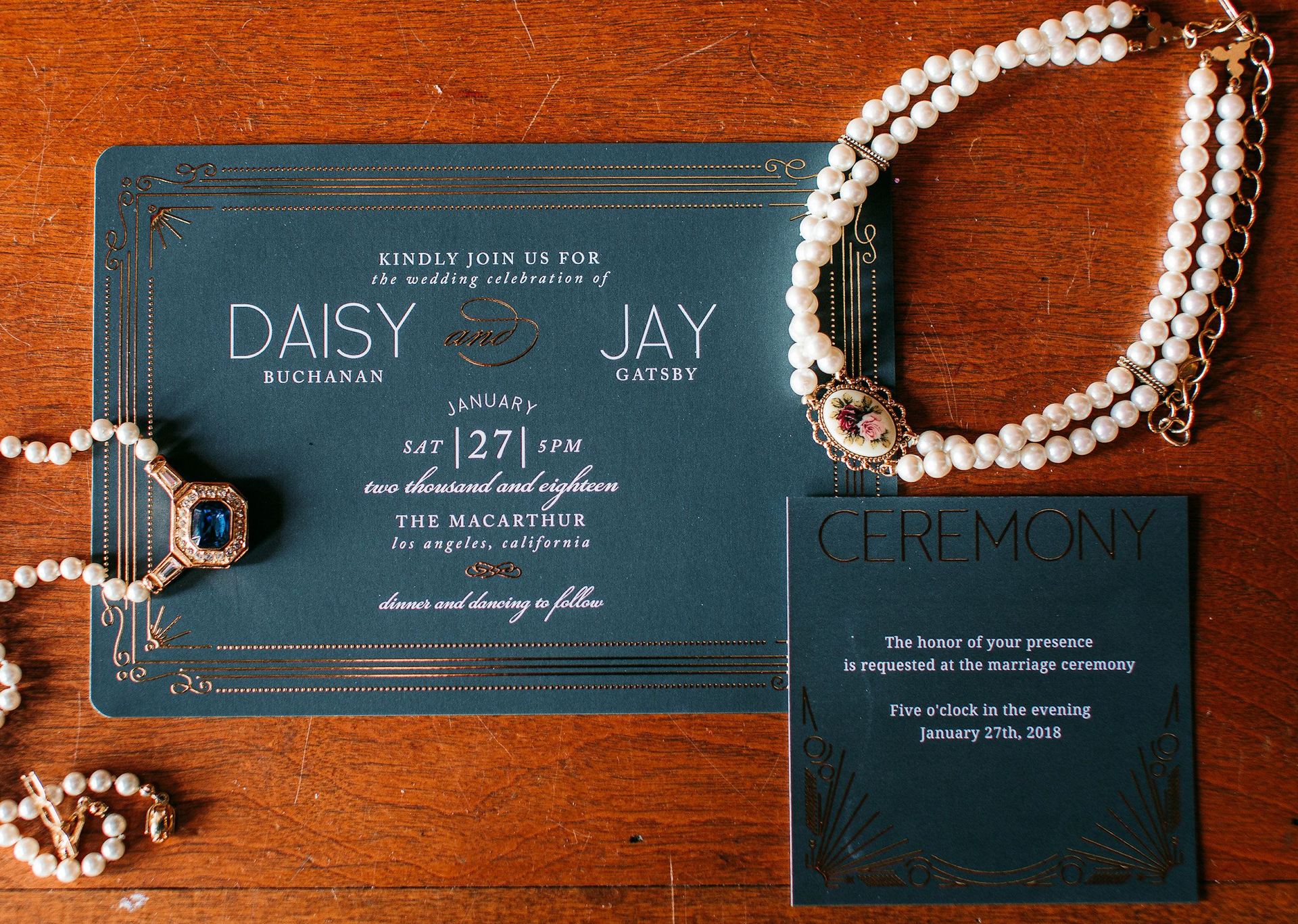 Navy wedding invitation surrounded by pearls laid upon wooden table
