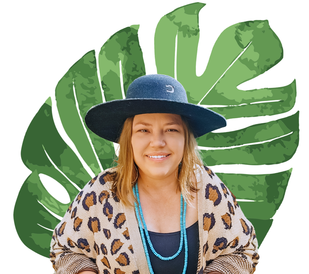 A woman wearing a hat and a leopard print cardigan is smiling in front of a green leaf.