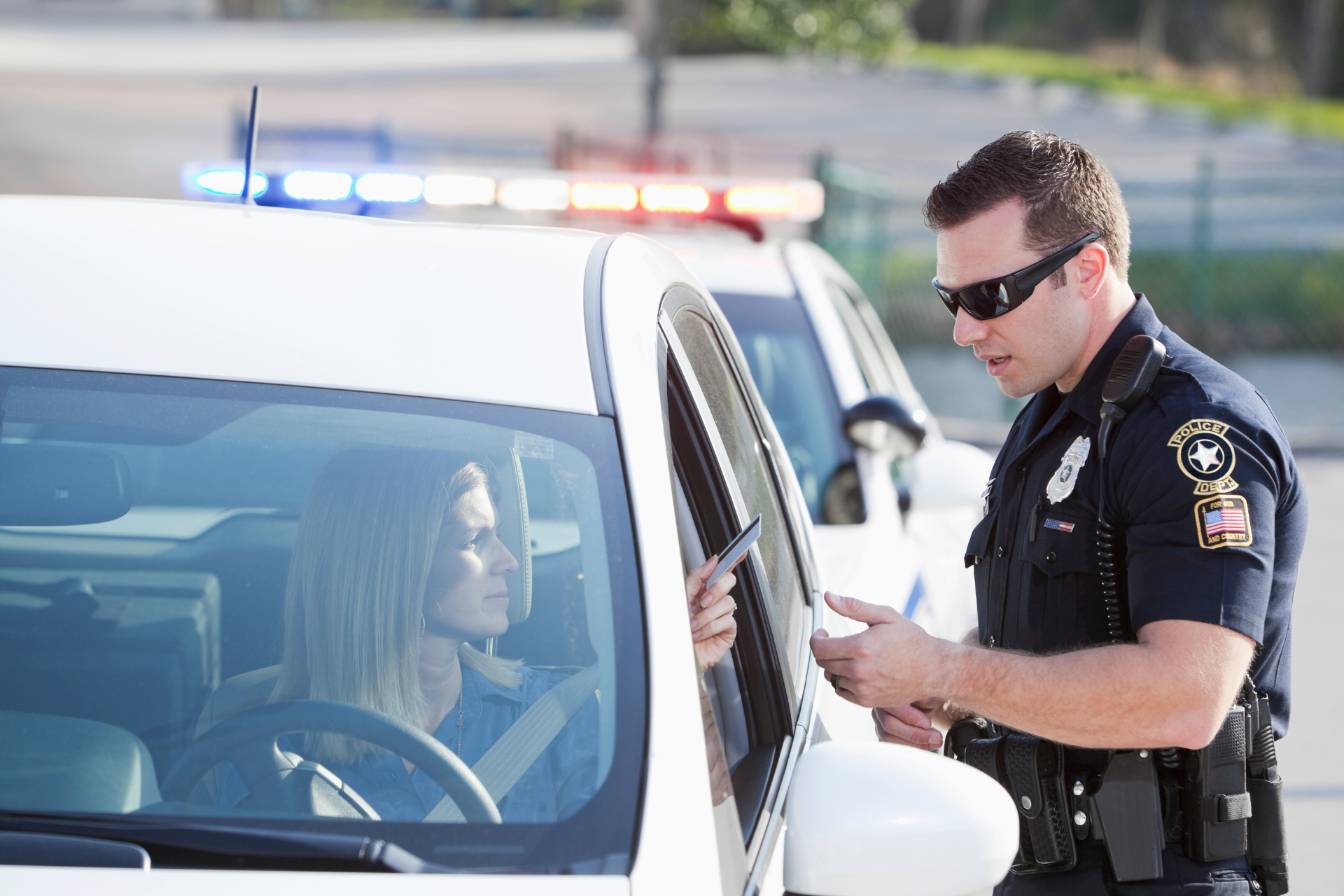 Police officer giving a ticket to a woman in a car; roadside stop.