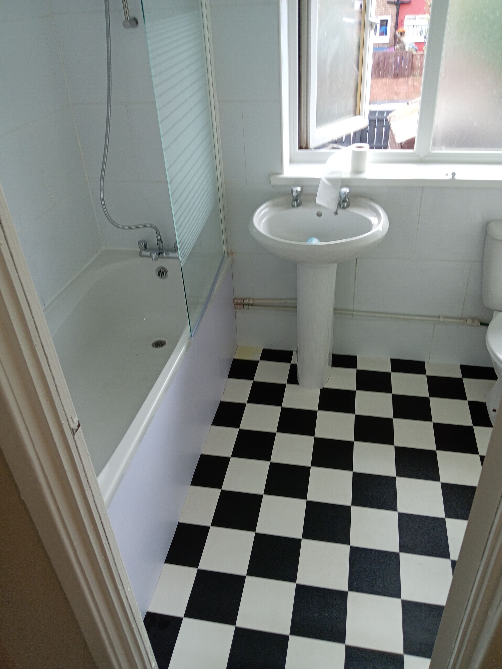Bathroom with black and white checkered floor, bathtub, pedestal sink, and window.