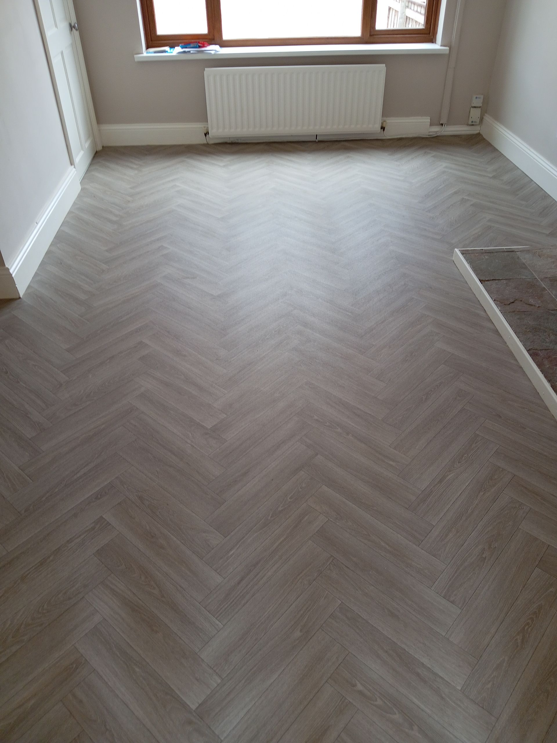 Herringbone pattern vinyl flooring in a room with a radiator and window.
