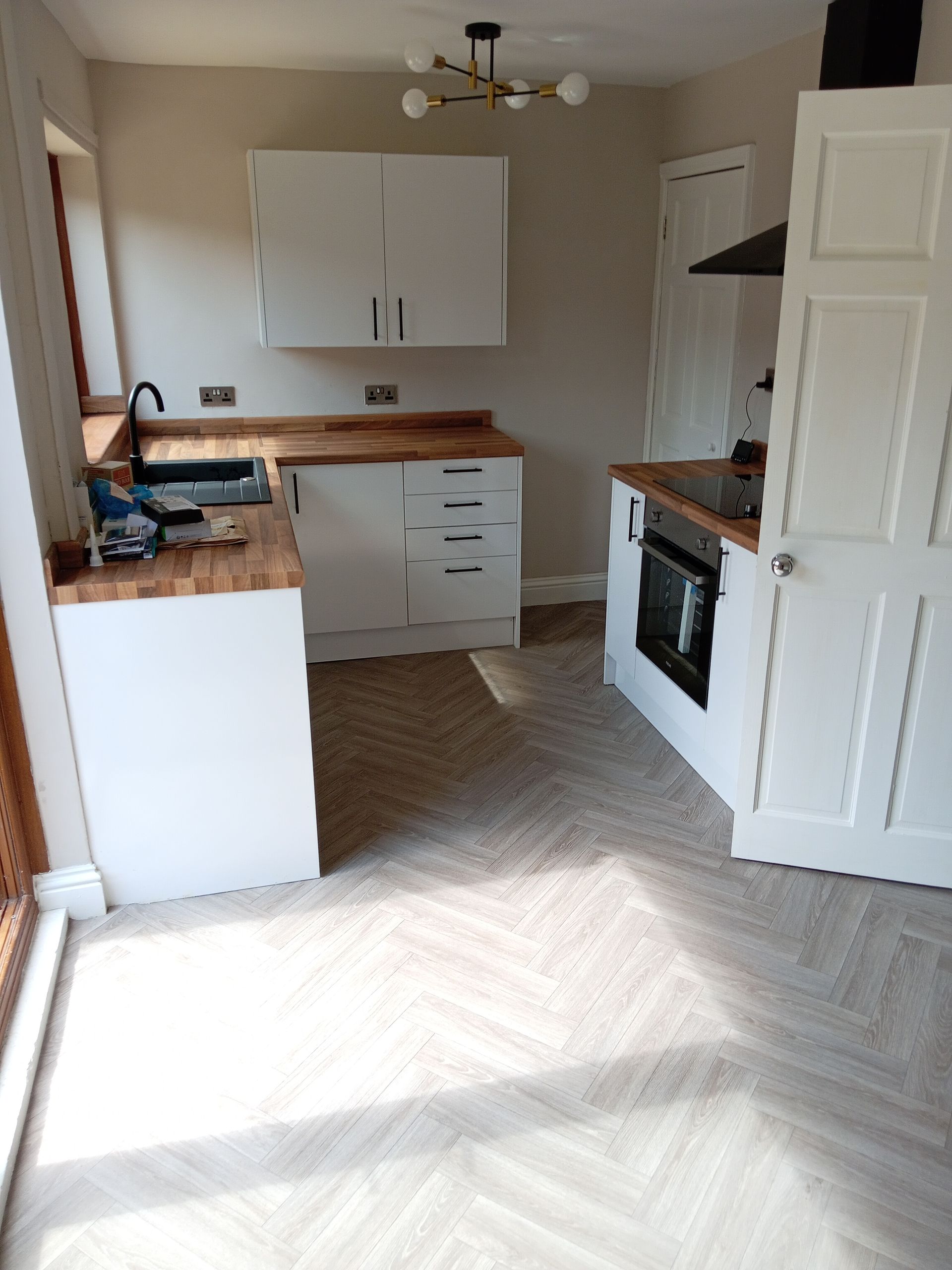 White kitchen with wooden counters, cabinets, and a black oven. Herringbone patterned floor.