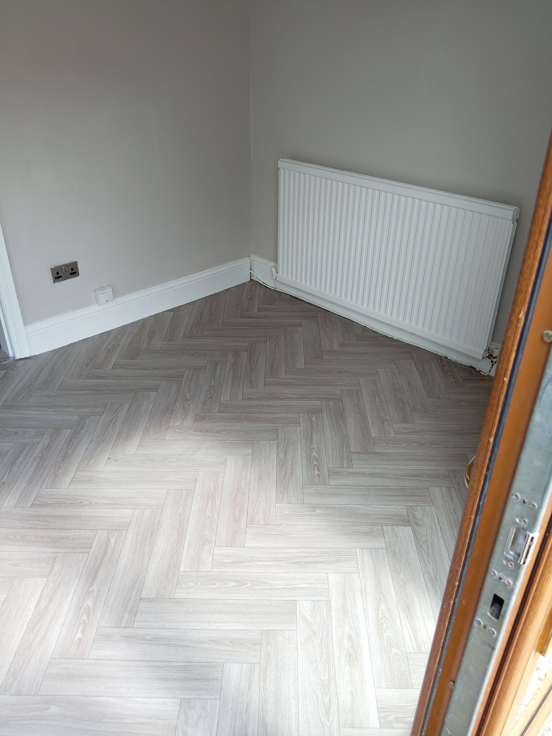 Corner of a room with beige walls, parquet flooring, and a radiator.