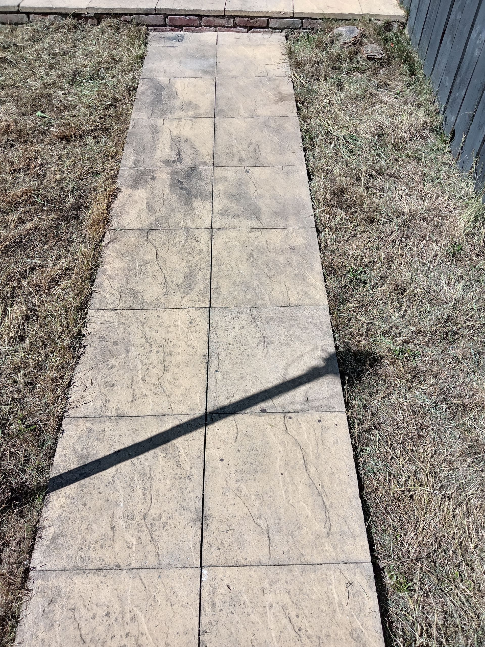 Stone walkway through dry grass, leading to a brick border.