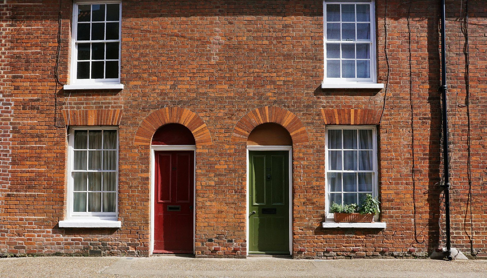 Brick building facade with red and green doors, white-framed windows.